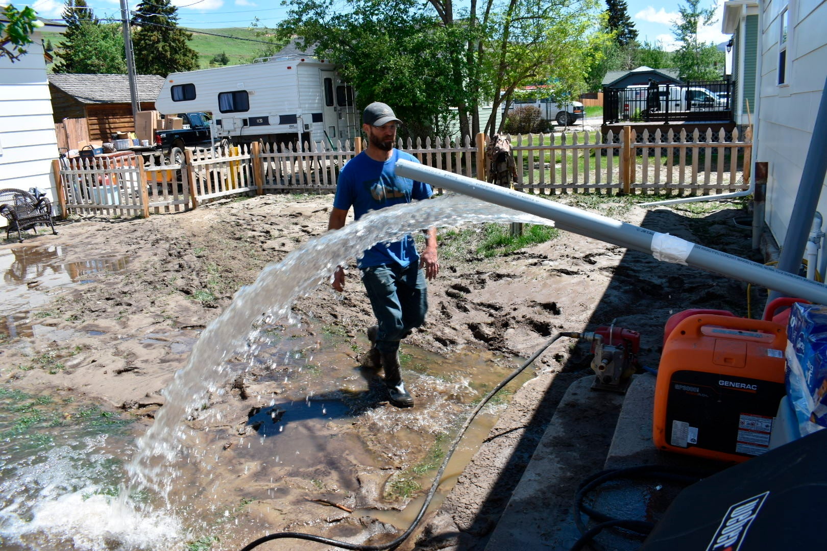 Micah Hoffman is seen in his mud-covered yard as a pump removes water  from his basement, Tuesday June 14, 2022, in Red Lodge, Mont.