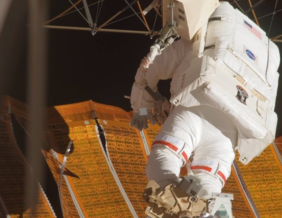 STS-120 astronaut Scott Parazynski standing atop the robotic arm and inspecting the tear in the solar array.