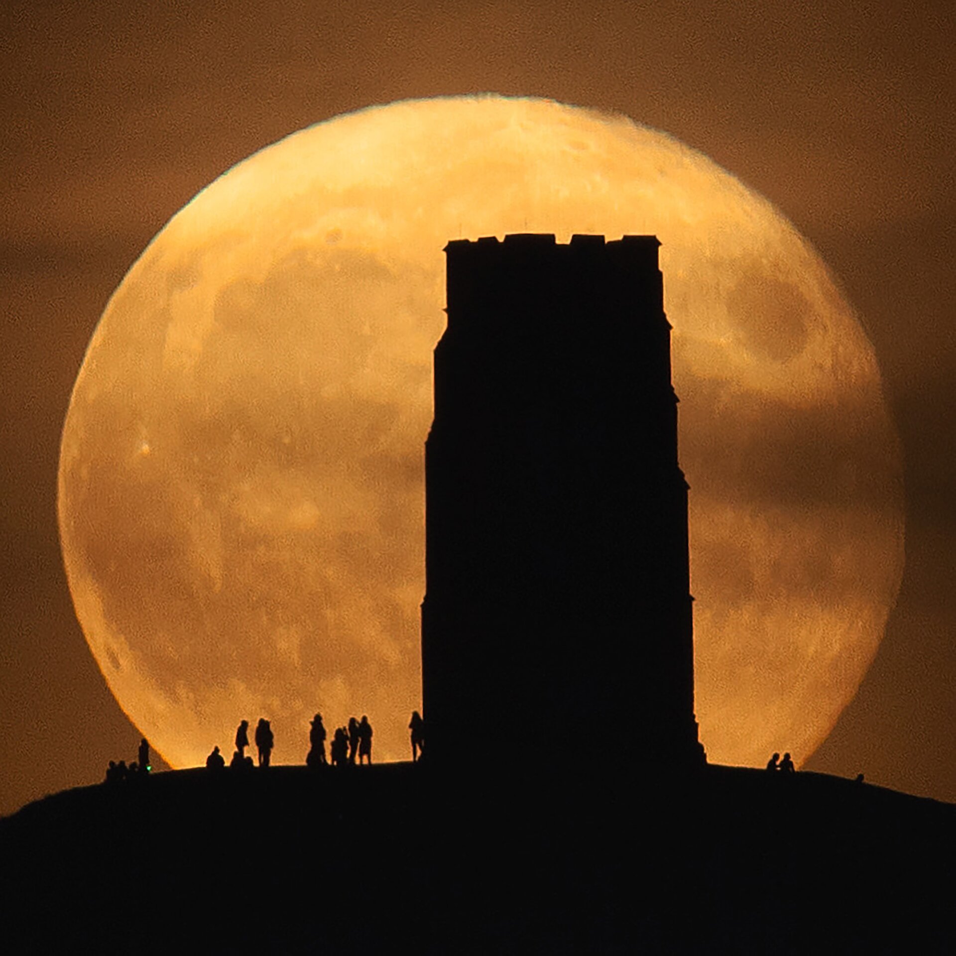 The bright orange harvest moon behind Glastonbury Tor (and onlookers).