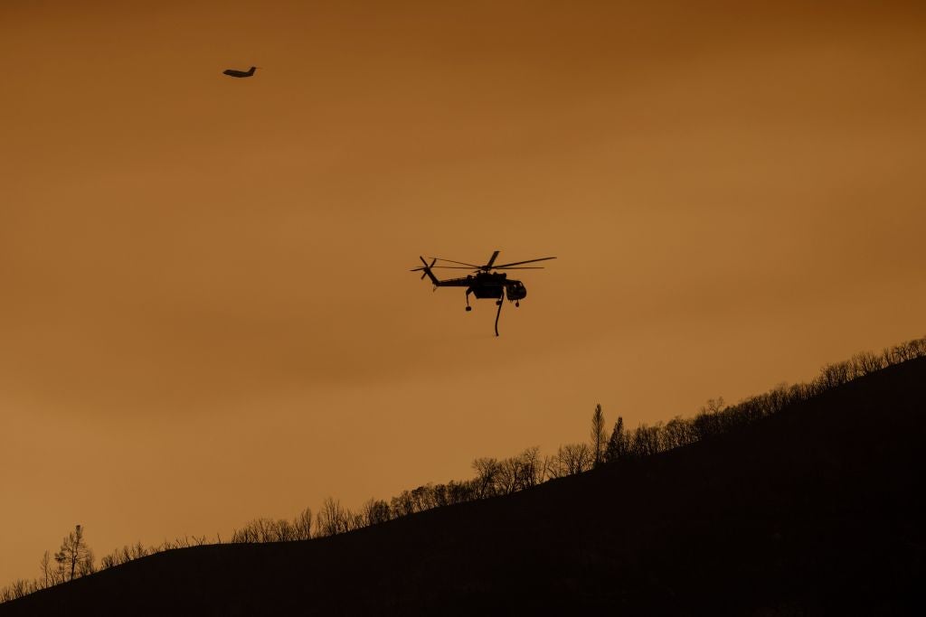 A firefighting aircraft fly through a smoke-filled sky near a burned ridge at the Oak Fire near Mariposa, California, on July 24, 2022.