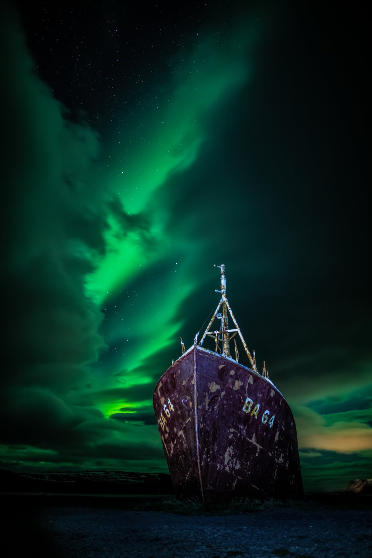 A shipwreck sits in the foreground, with the Northern Lights above it. 