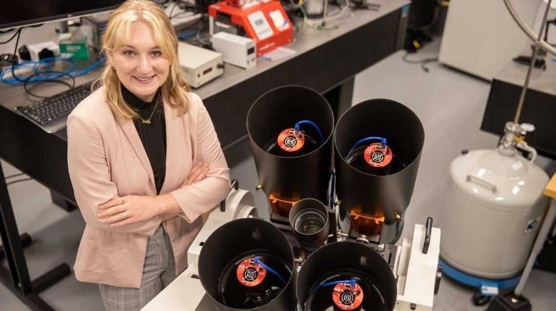University of Arizona student Grace Halferty stands next to the instrument developed by her team to measure satellite brightness.