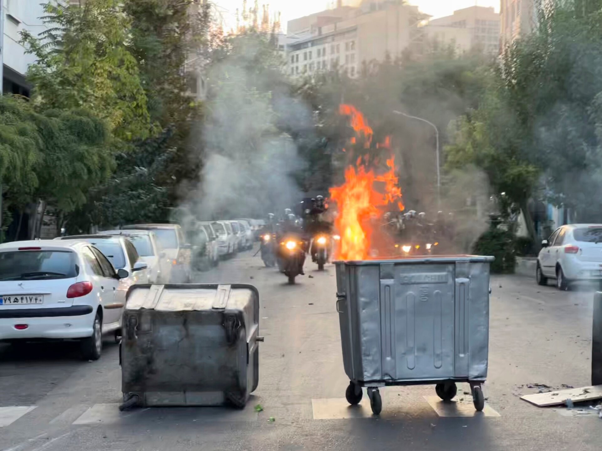 In this Tuesday, Sept. 20, 2022, photo taken by an individual not  employed by the Associated Press and obtained by the AP outside Iran, a  trash bin is burning as anti-riot police arrive during a protest over  the death of a young woman who had been detained for violating the  country’s conservative dress code, in downtown Tehran, Iran.