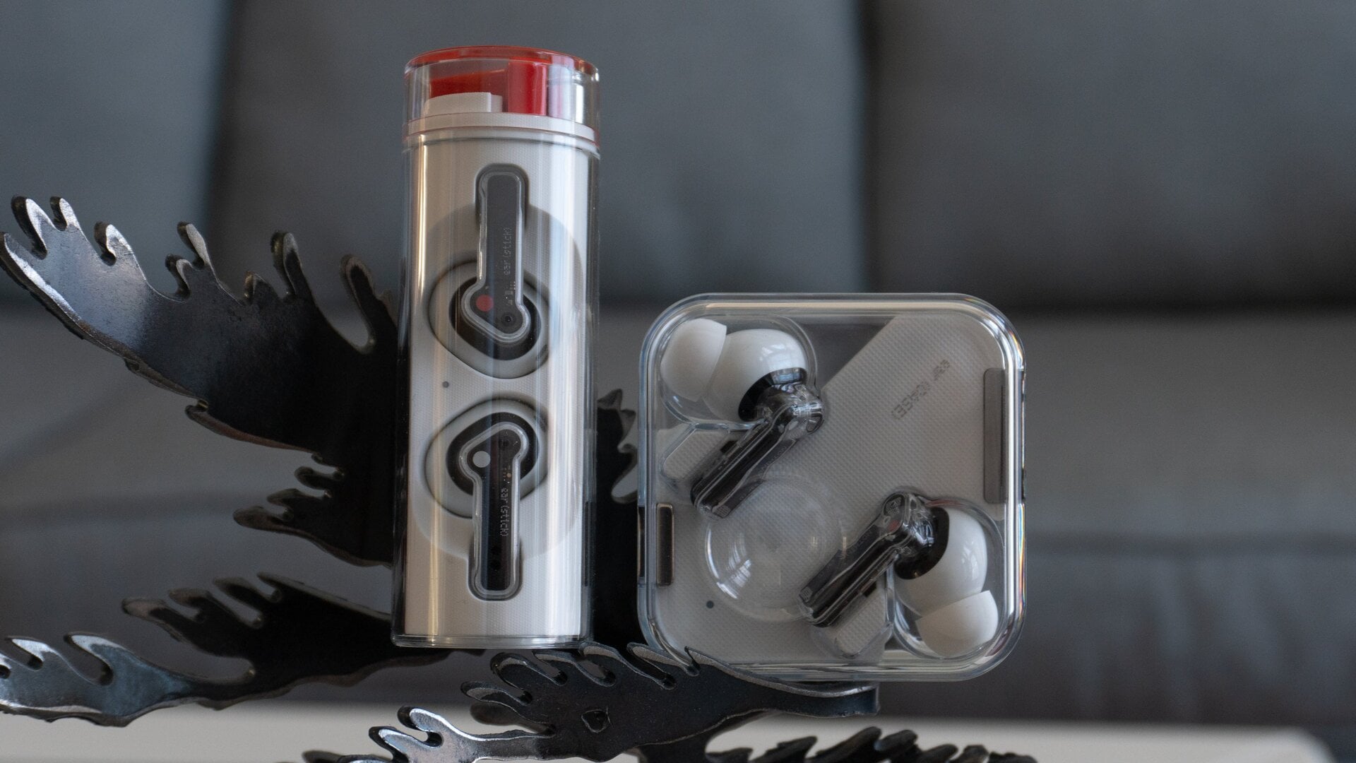 The Nothing Ear (stick) in their cylindrical charging case (left) next to the Nothing Ear (1) in their smaller charging case (right).