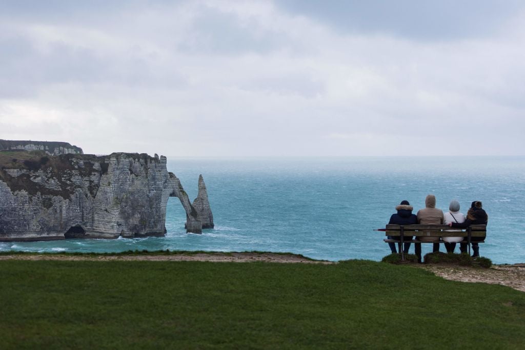 People sit on bench looking at a natural arch and the chalk cliffs in Etretat on January 4, 2022. 