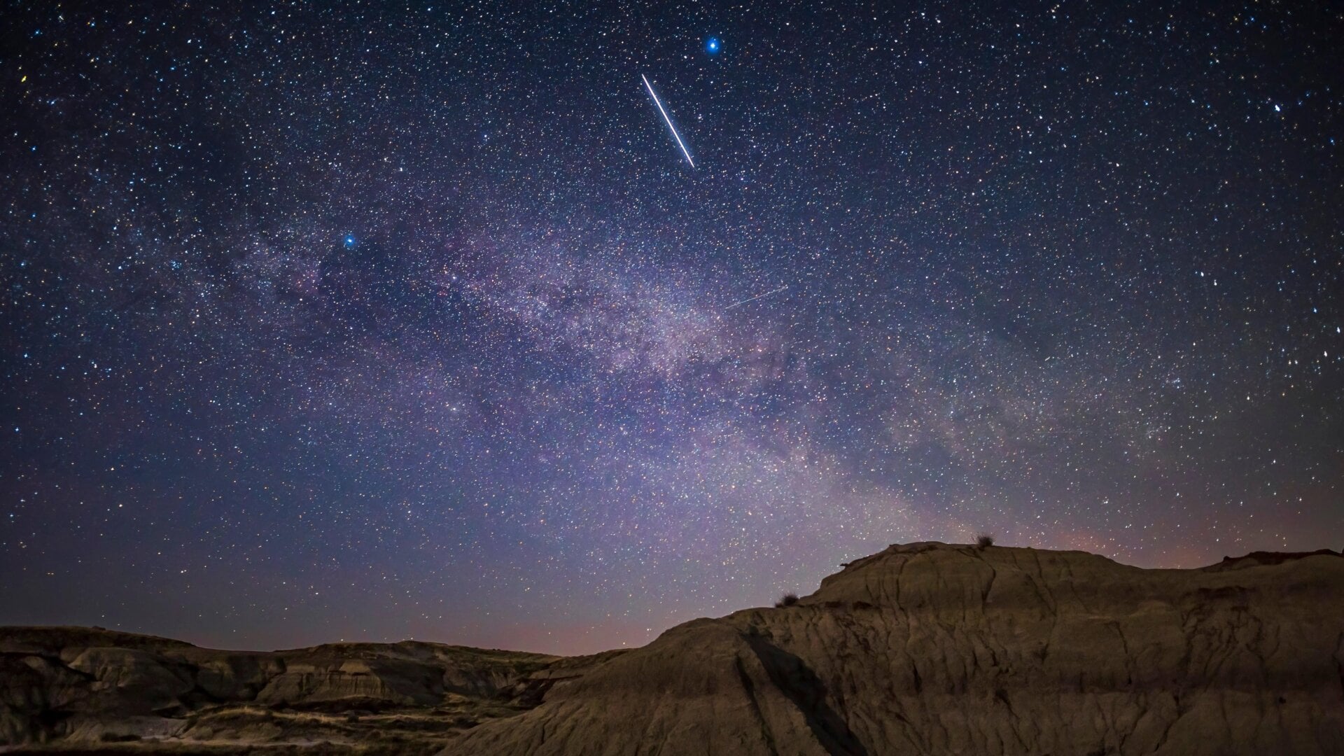 The Starlink 27 satellites, visible as a bright line in the sky over Dinosaur Provincial Park in Alberta, Canada on the same day as their 2021 launch from Cape Canaveral.