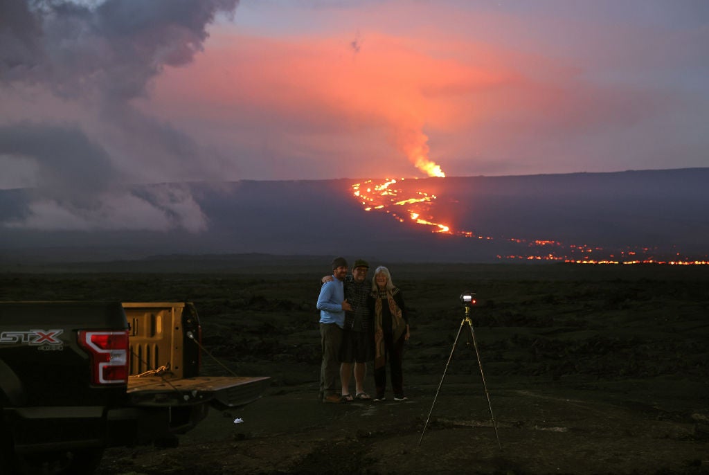 A group of people take a photo as the Mauna Loa volcano erupts behind them on December 04, 2022 near Hilo, Hawaii.