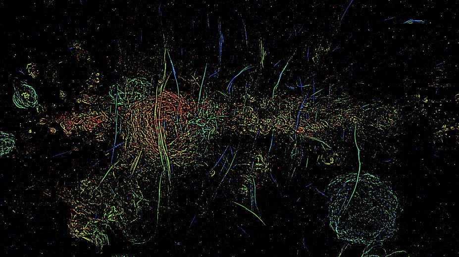 A multi-colored image shows long vertical streaks of magnetic filaments in the Milky Way’s core.