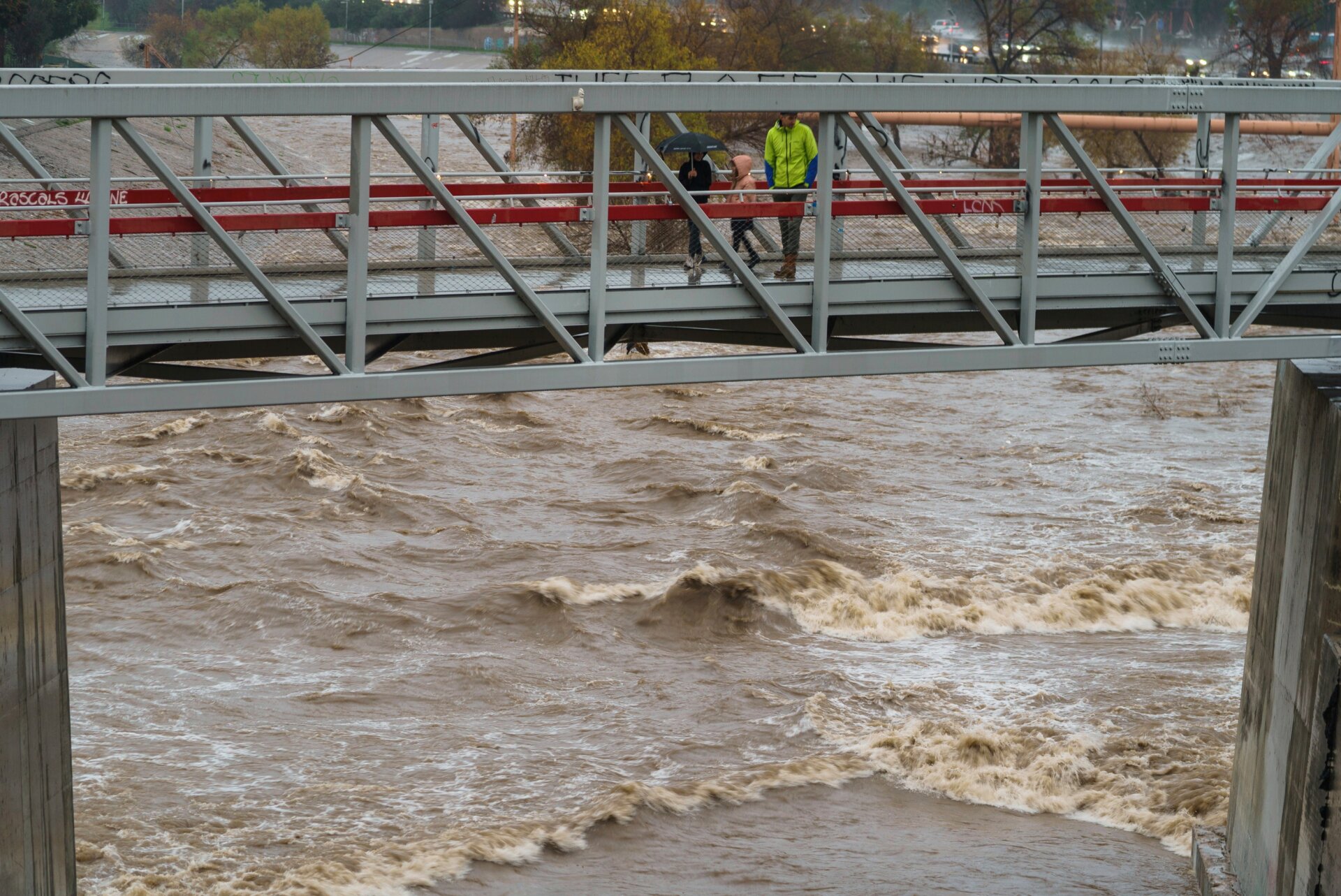 People cross a bridge over a swollen Los Angeles River in Los Angeles on Saturday, January. 14, 2023. 