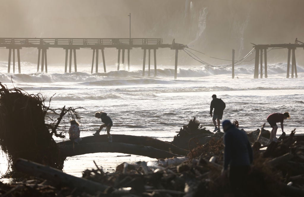 People gather near storm debris washed up on the beach, with a storm-damaged pier in the background, on January 10, 2022 in Capitola, California. 