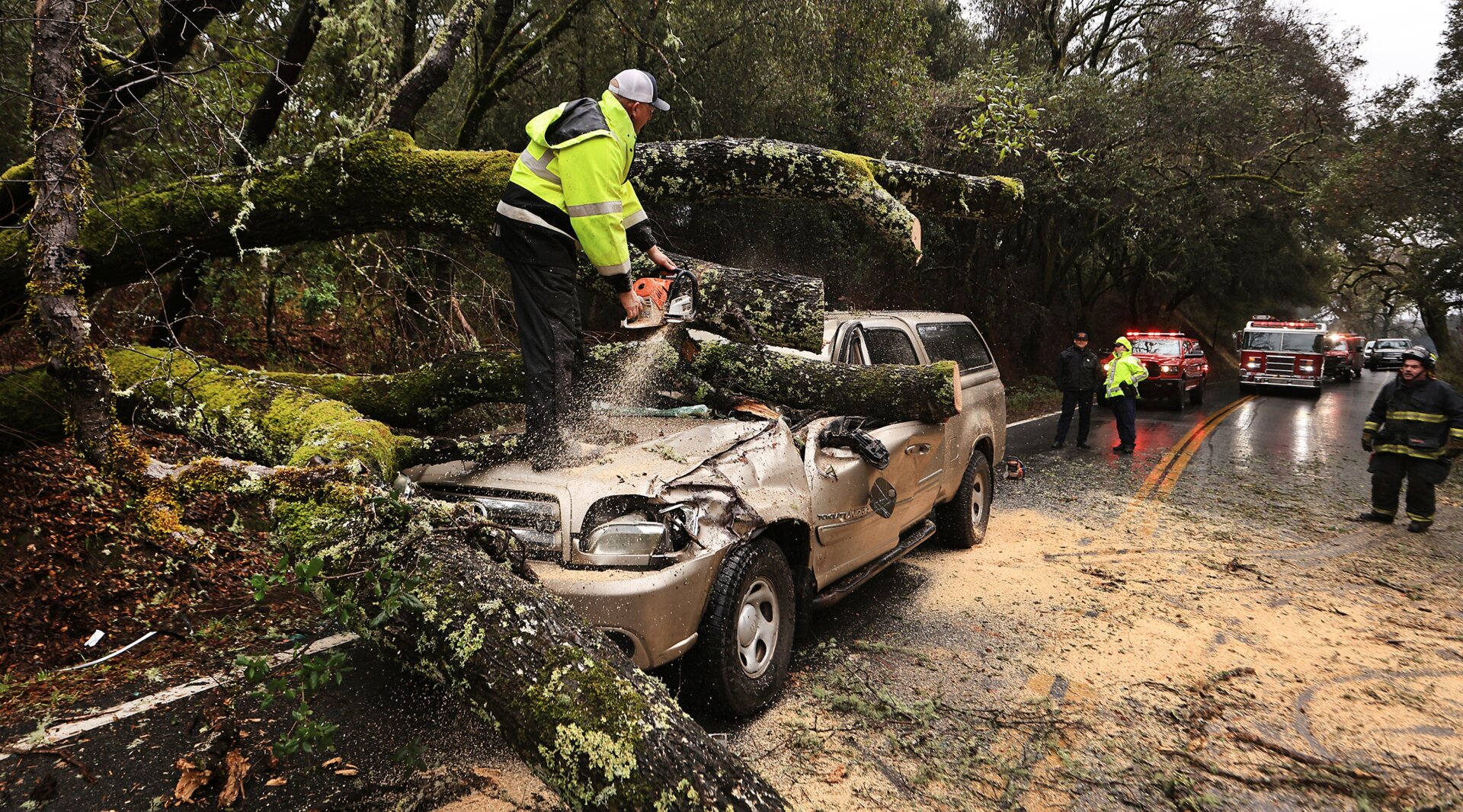 Hopland Volunteer Fire Department chief Mitch Franklin cuts away a large oak tree that fell on a vehicle, moderately injuring the driver on Old River Road, north of Hopland, Calif., in Mendocino County, Saturday, January. 14, 2023.