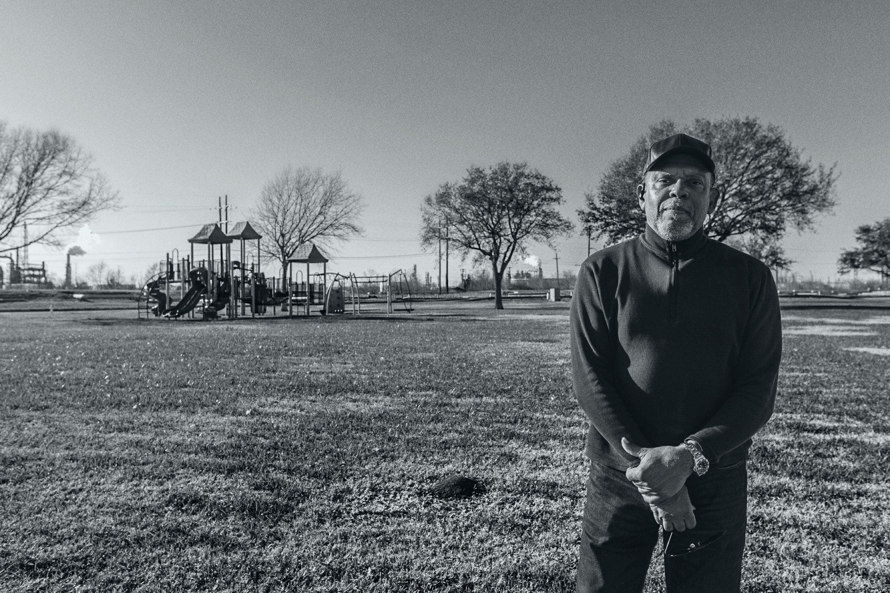 John Beard poses at Carver Terrace Park in Port Arthur, with refinery smokestacks visible less than half a mile away.