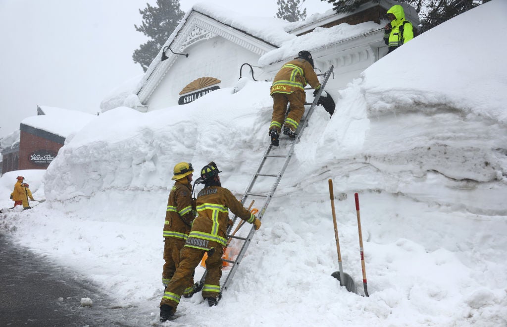 Mammoth Lakes Fire Department firefighters use a ladder on a snowbank while responding to a propane heater leak and small fire at a shuttered restaurant surrounded by snowbanks on March 12, 2023 in Mammoth Lakes, California. 