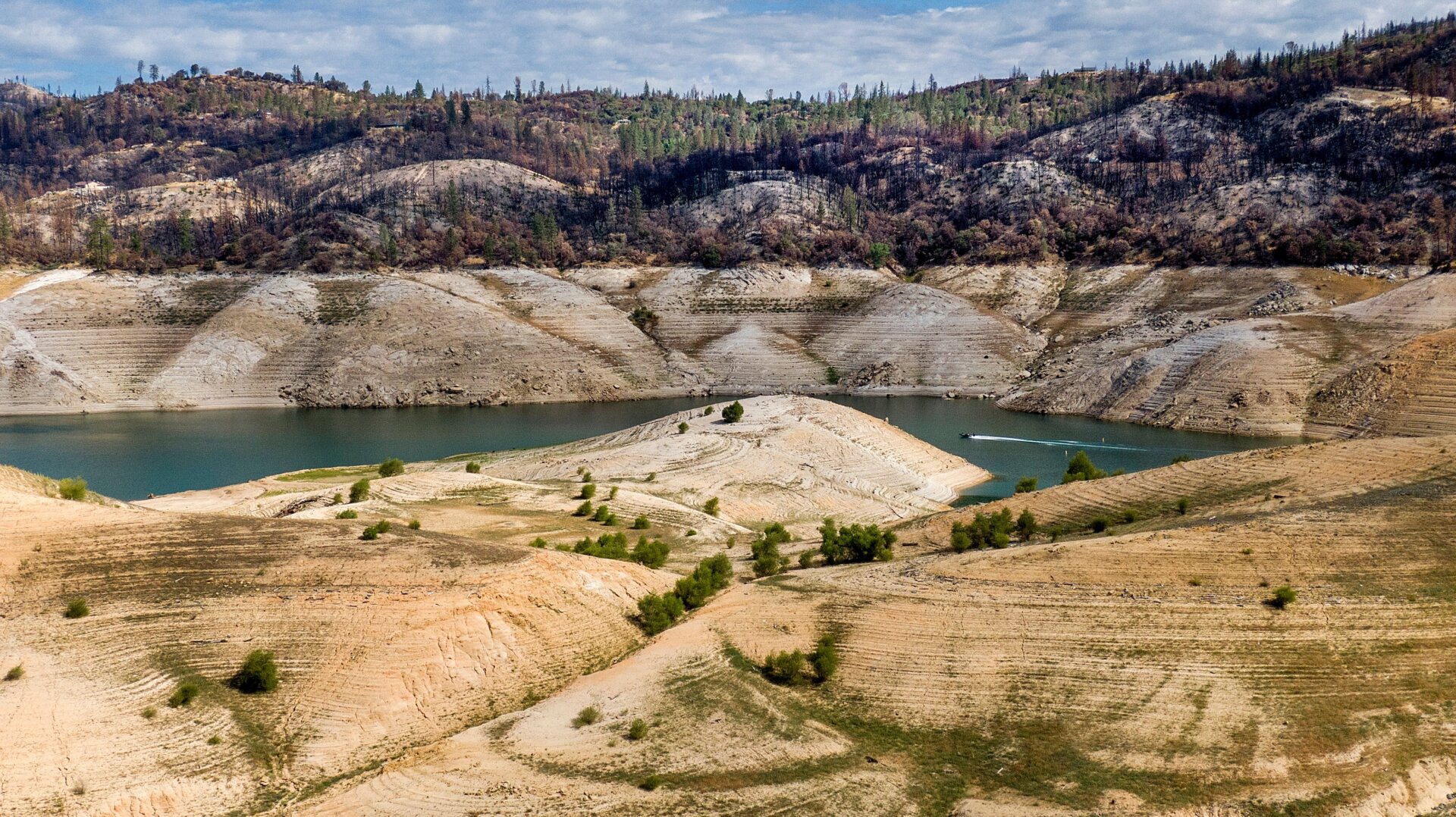 A boat crosses Lake Oroville below trees scorched in the 2020 North Complex Fire on May 23, 2021, in Oroville, California. 