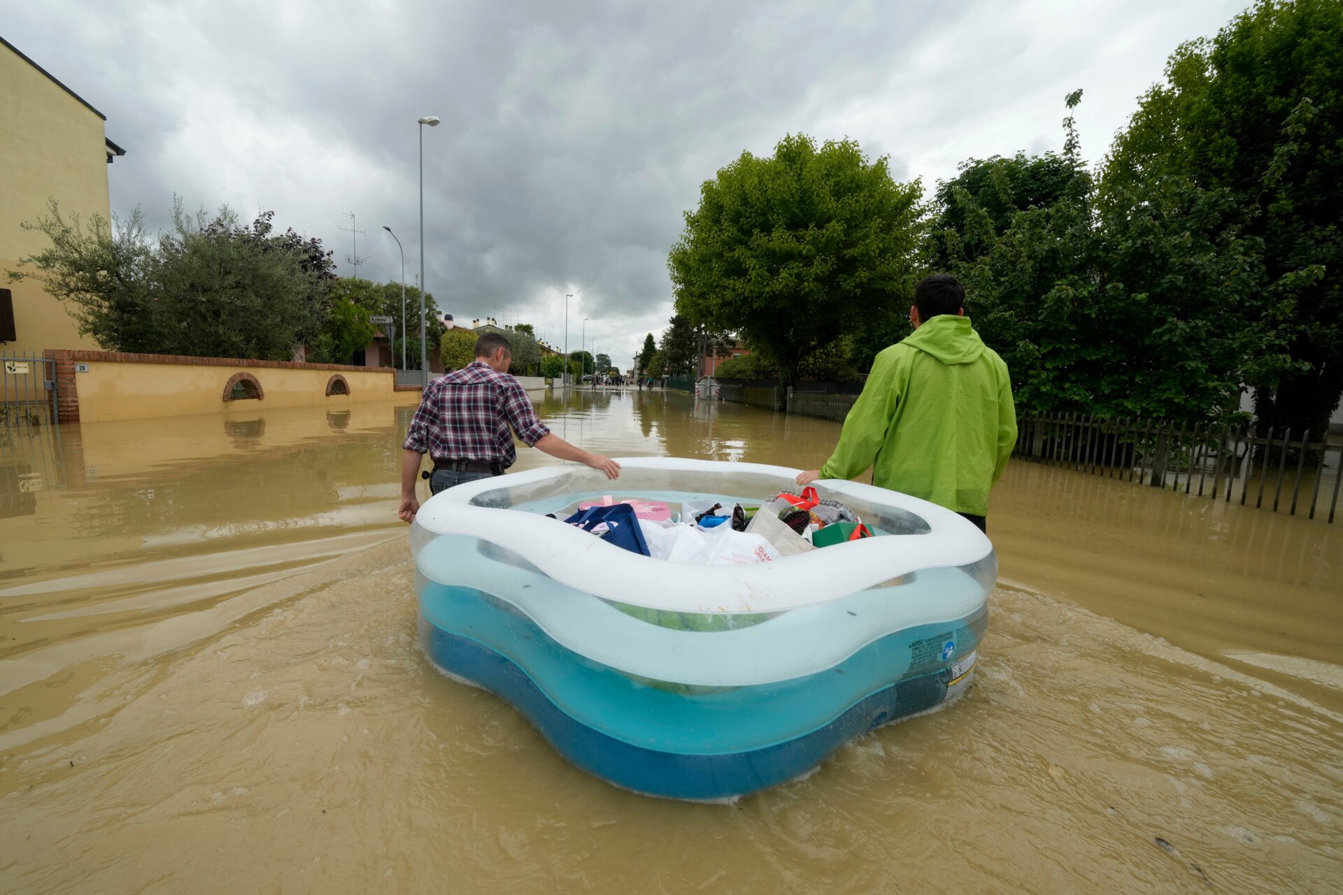 People use a plastic, inflatable kiddie pool to carry their belongings down a flooded road in Lugo Italy on May 18. Floodwaters and mud inundated many peoples’ homes. 