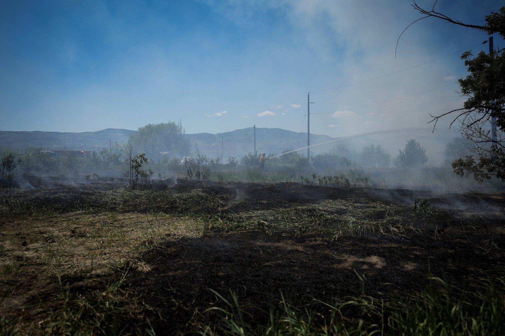 A firefighter directs water on a grass fire on an acreage behind a residential property in Kamloops, British Columbia, on June 5, 2023.