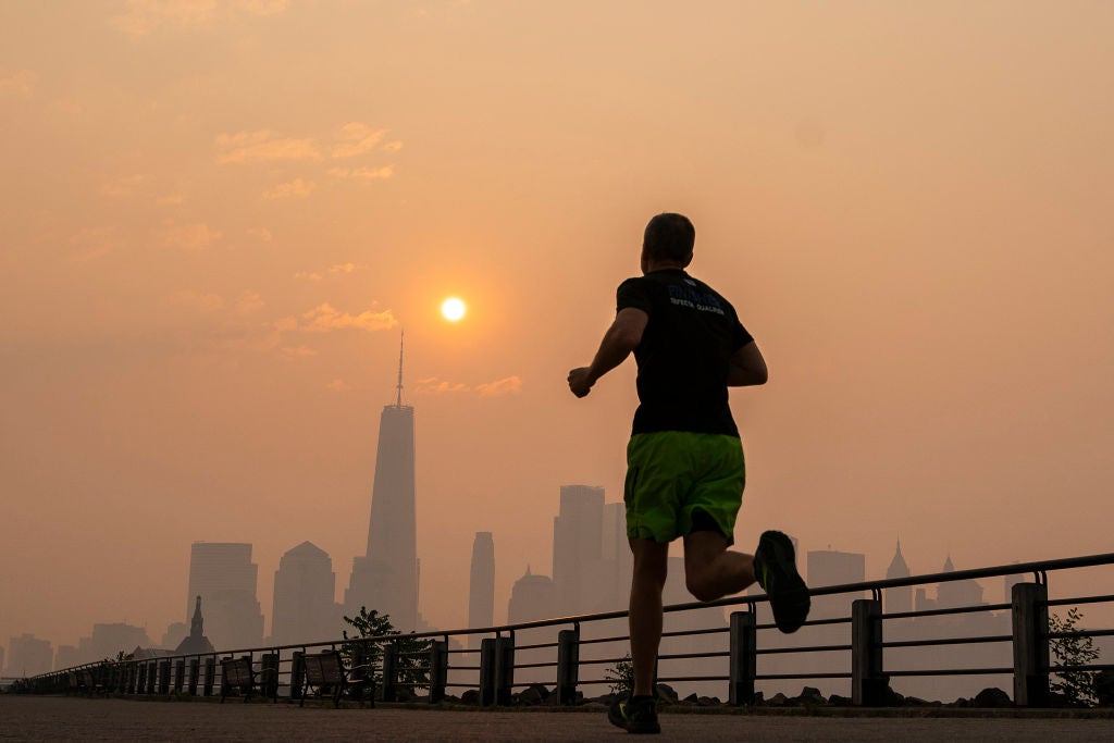 The One World Trade Center and the New York skyline is seen in the background as a man jogs, while the smoke from Canada wildfires covers area on June 8, 2023 in New Jersey. 