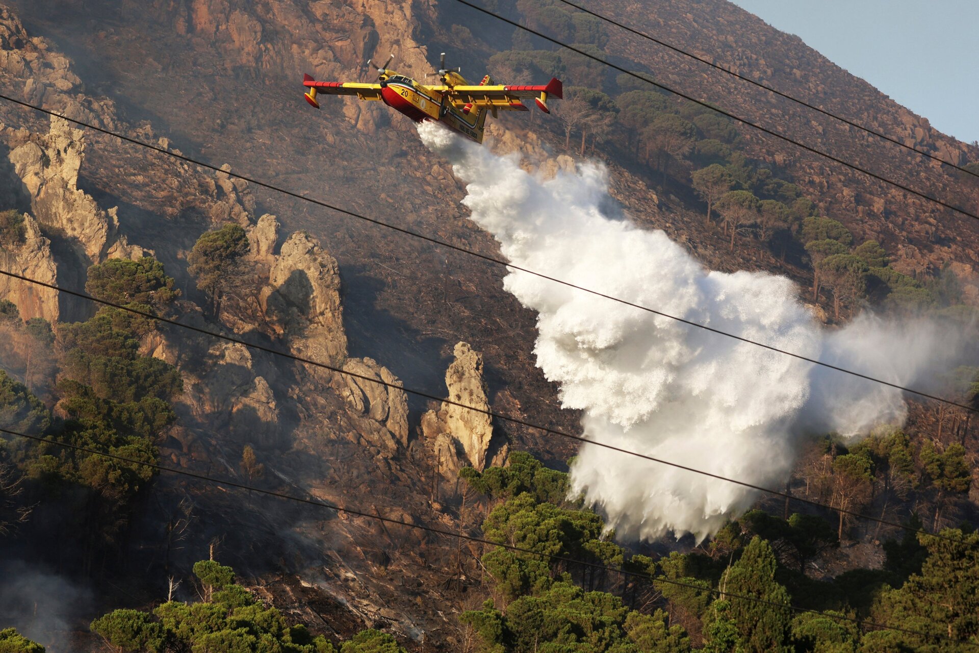 A firefighting plane drains water on a wildfire on the mountain in Altofonte near Palermo, Italy, Wednesday, July 26, 2023.
