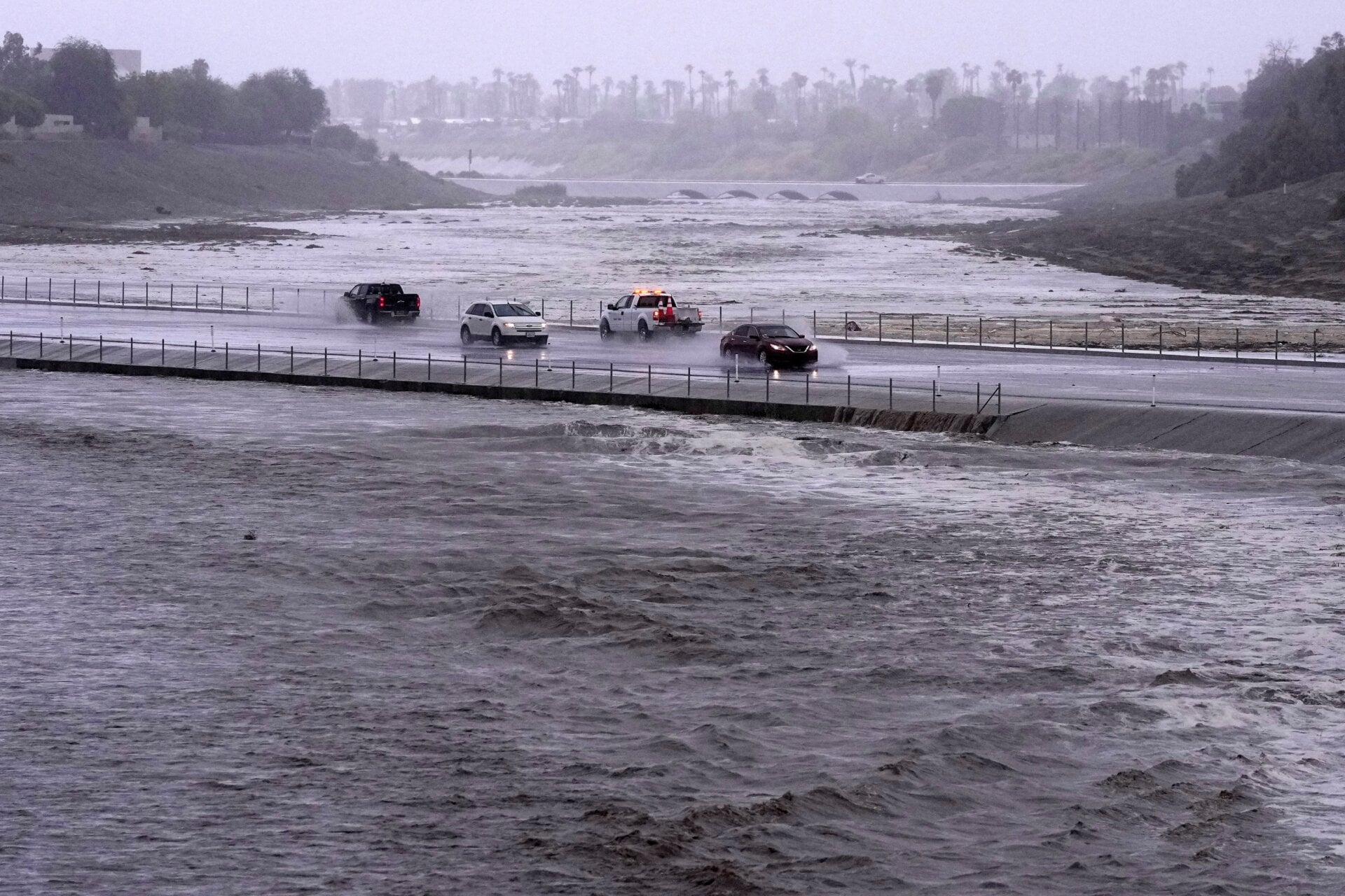 Vehicles cross over a flood control basin that has almost reached the street, on Sunday, August. 20, 2023, in Palm Desert, California. 