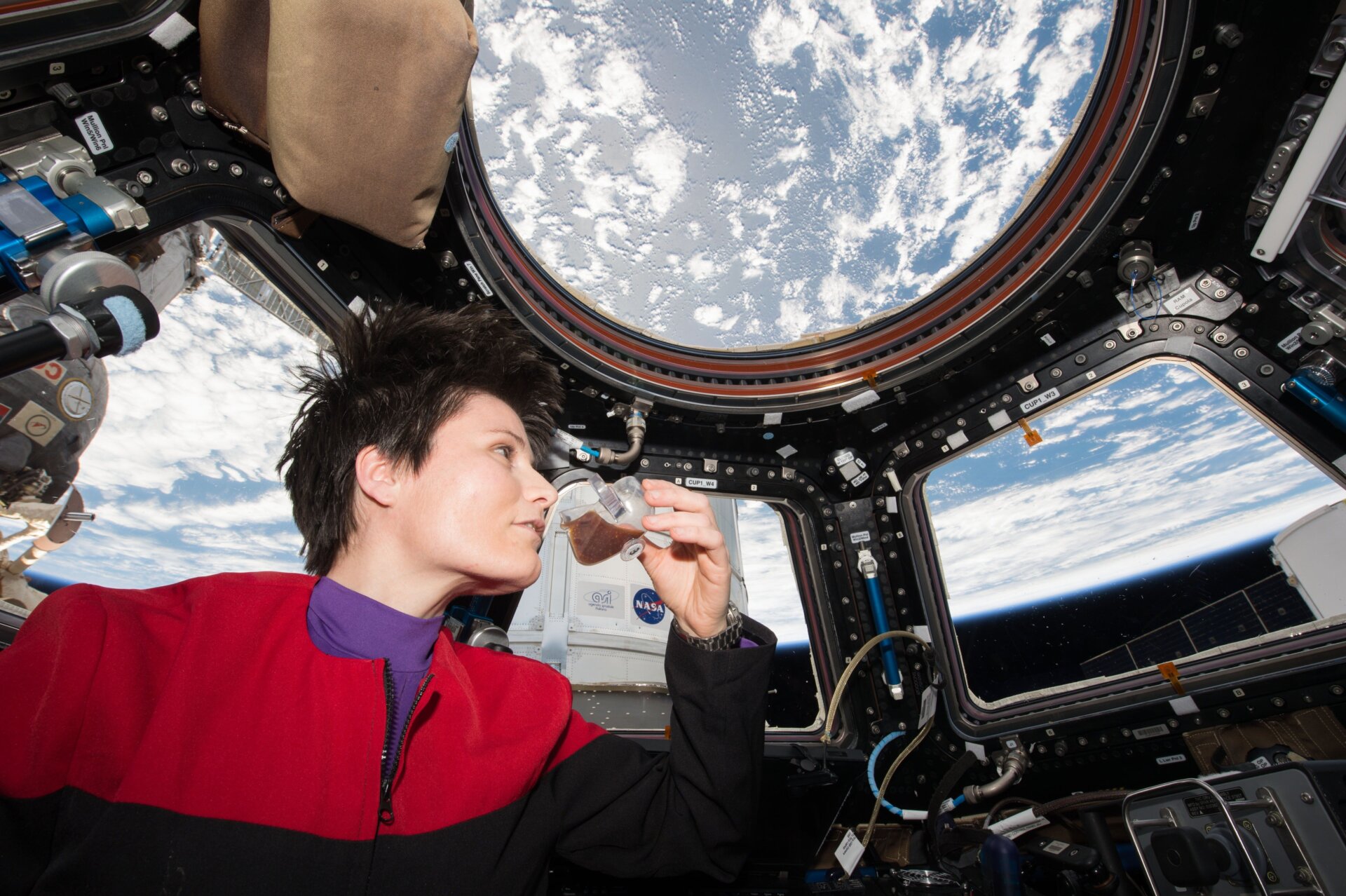 European Space Agency (ESA) astronaut Samantha Cristoforetti, donning a uniform inspired by the Star Trek: Voyager series, enjoys a cup of espresso while gazing out of the Cupola window aboard the ISS.