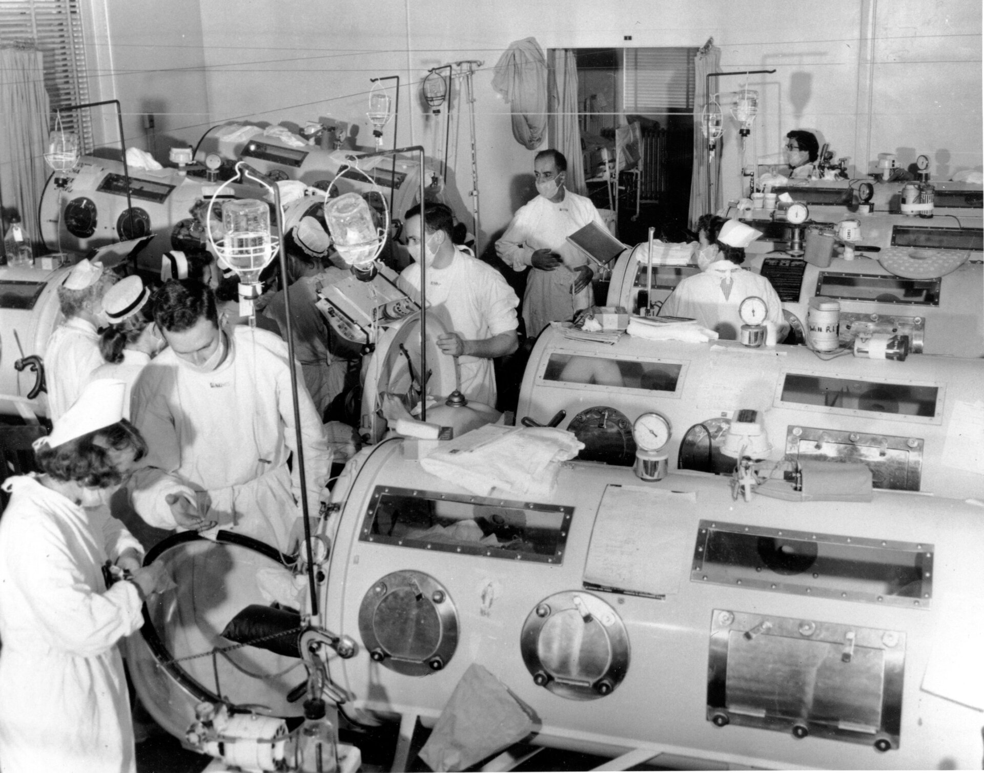 This is a scene in the emergency polio ward at Haynes Memorial Hospital  in Boston, MA., on Aug. 16, 1955. The city’s polio epidemic hit a high  of 480 cases. The critical patients are lined up close together in iron  lung respirators so that a team of doctors and nurses can give fast  emergency treatment as needed. 