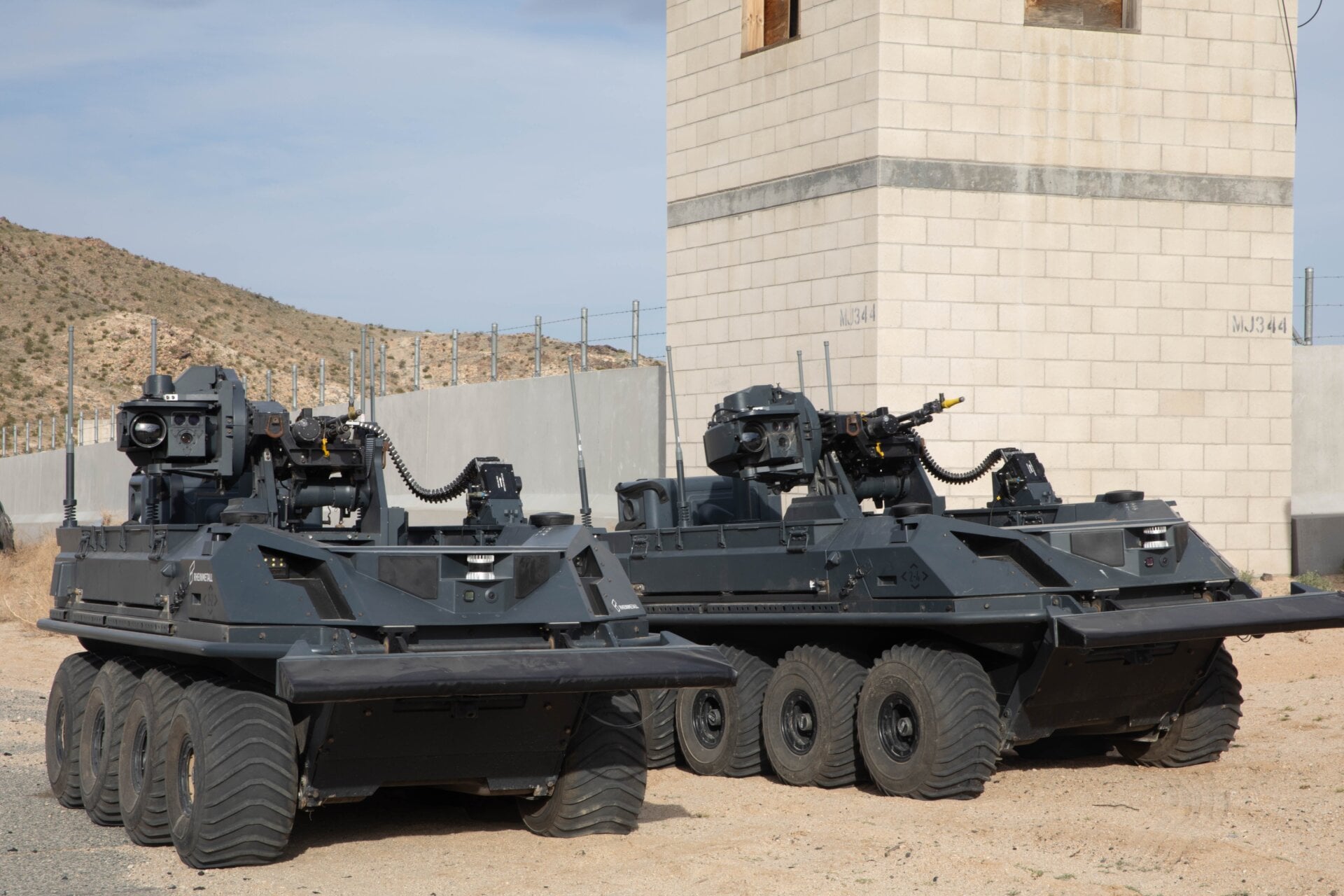 Two British unmanned, eight-wheeled, all-electric, all-terrain transport  vehicles armed with autonomous weapon system from the Experimentation  and Trails Group provide support to dismounted U.K. Soldiers in an urban  environment as part of a human integration experiment at Fort Irwin,  Calif, March 11, 2024.
