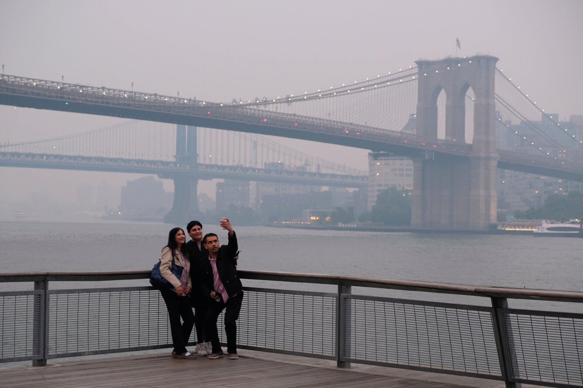 A group takes a selfie with the background of the Manhattan Bridge and  Brooklyn Bridge, right, in New York on Wednesday, June 7, 2023