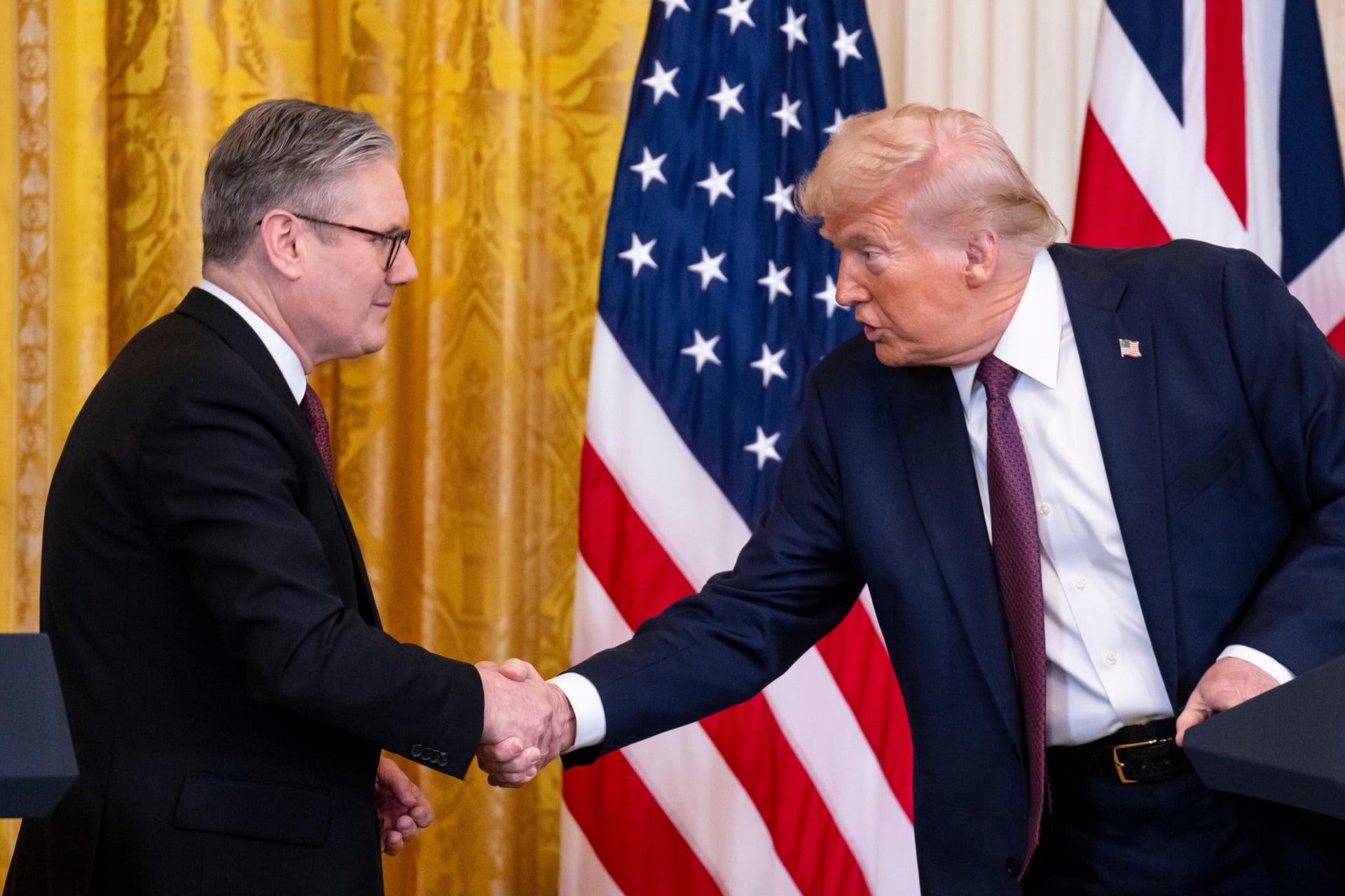 Donald Trump shaking hands with British Prime Minister Keir Starmer at a press conference, with the American and British flags in the background