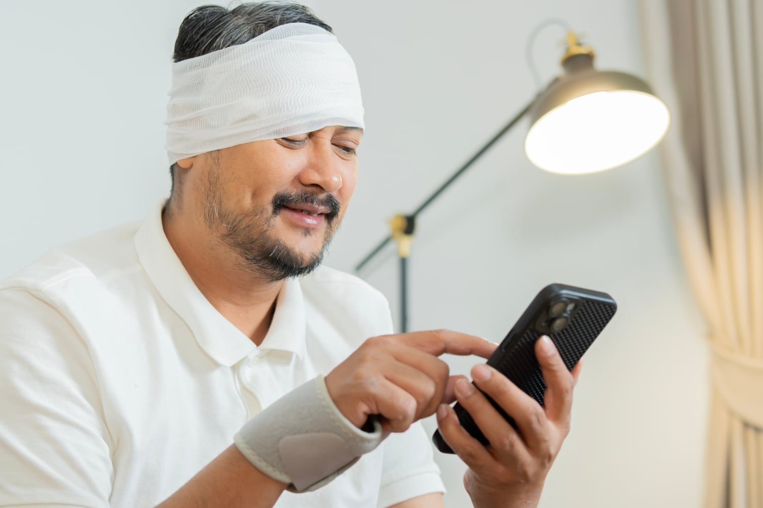 4. Stock photo of a man with a head injury smiling while using a smartphone