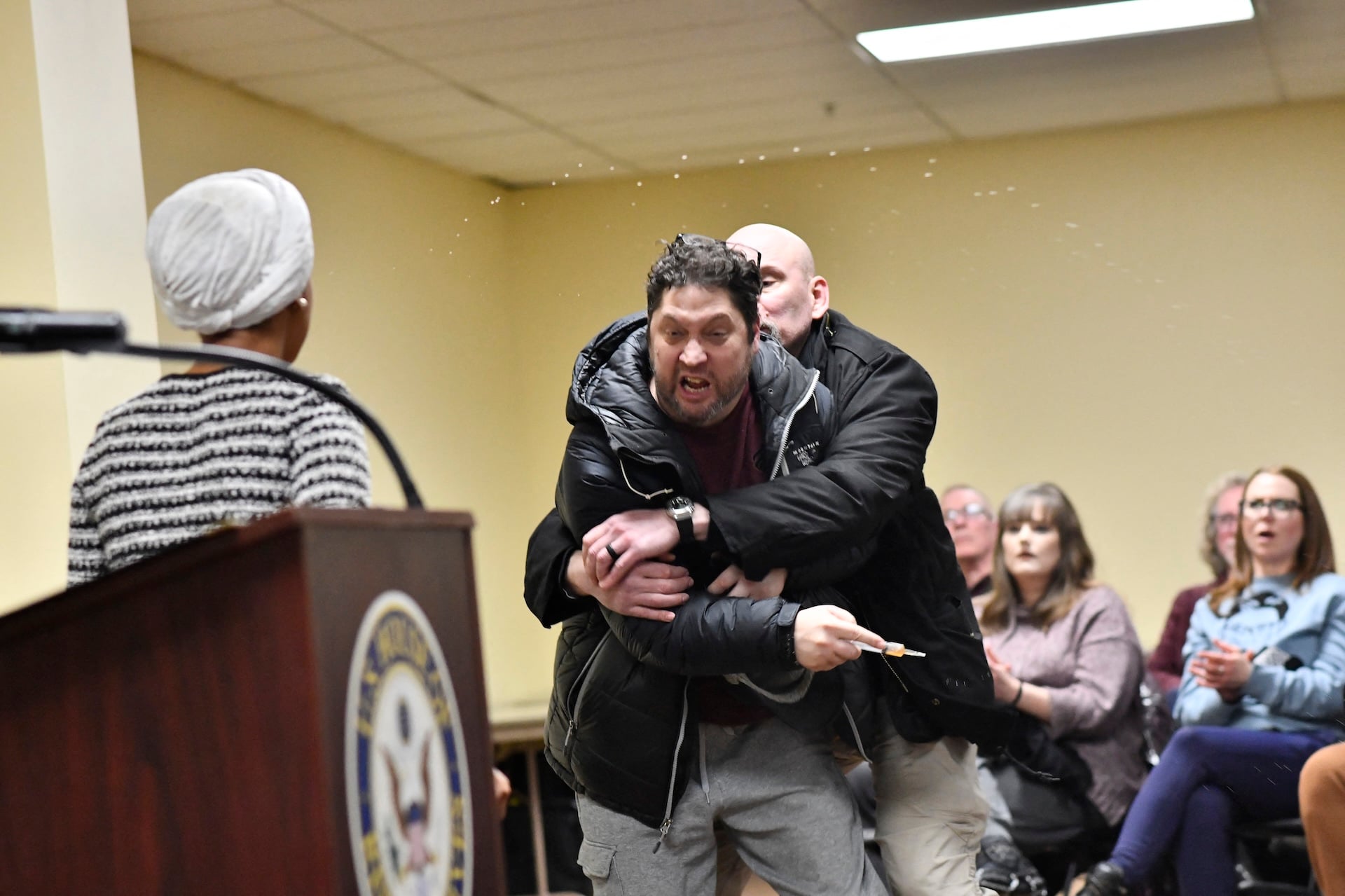 A man is tackled after spraying an unknown substance at US Representative Ilhan Omar (D-MN) (L) during a town hall she was hosting in Minneapolis, Minnesota, on January 27, 2026.