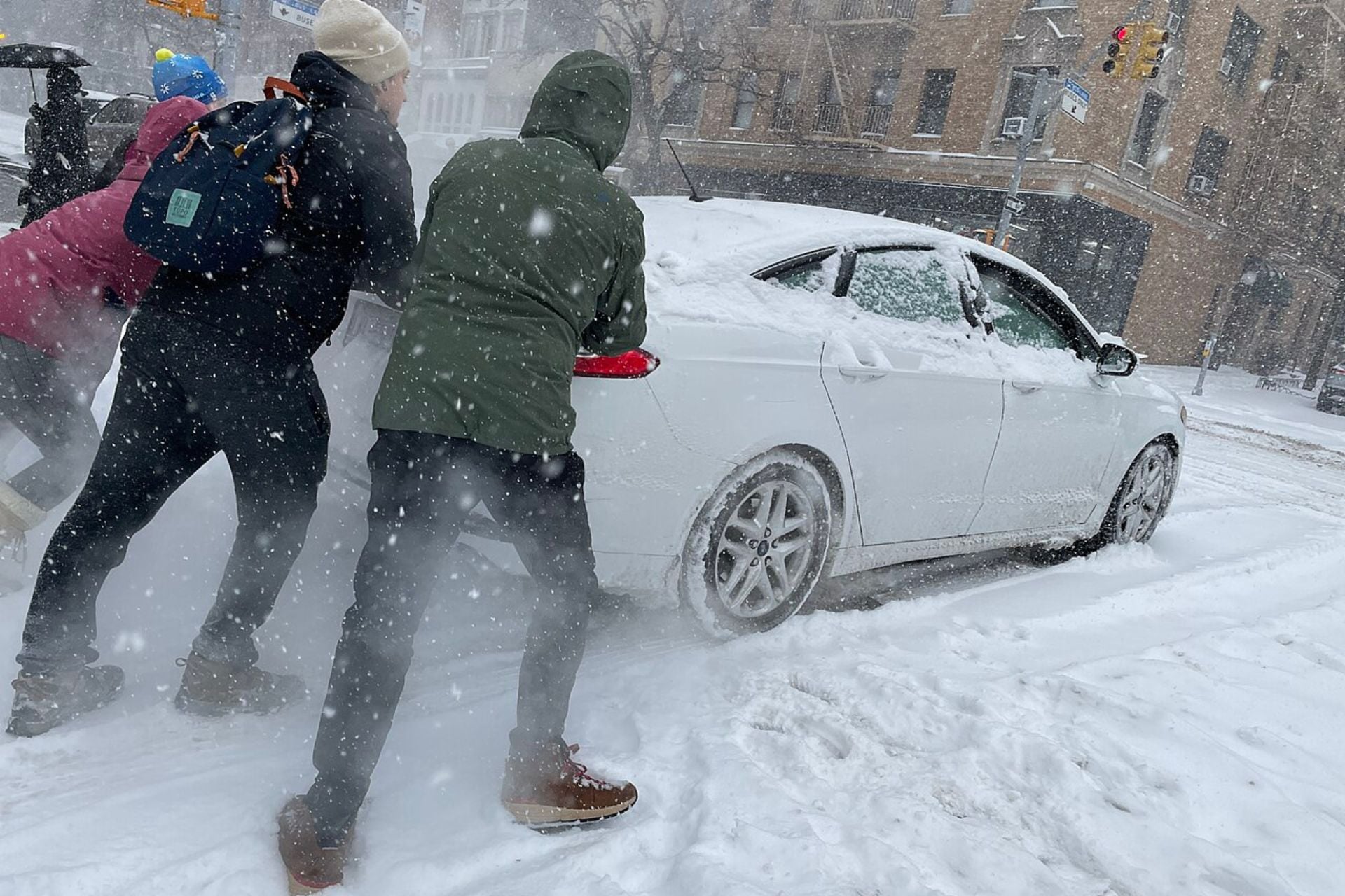 People push a car stuck in the snow on the Upper East Side of Manhattan during a major winter storm on January 25, 2026