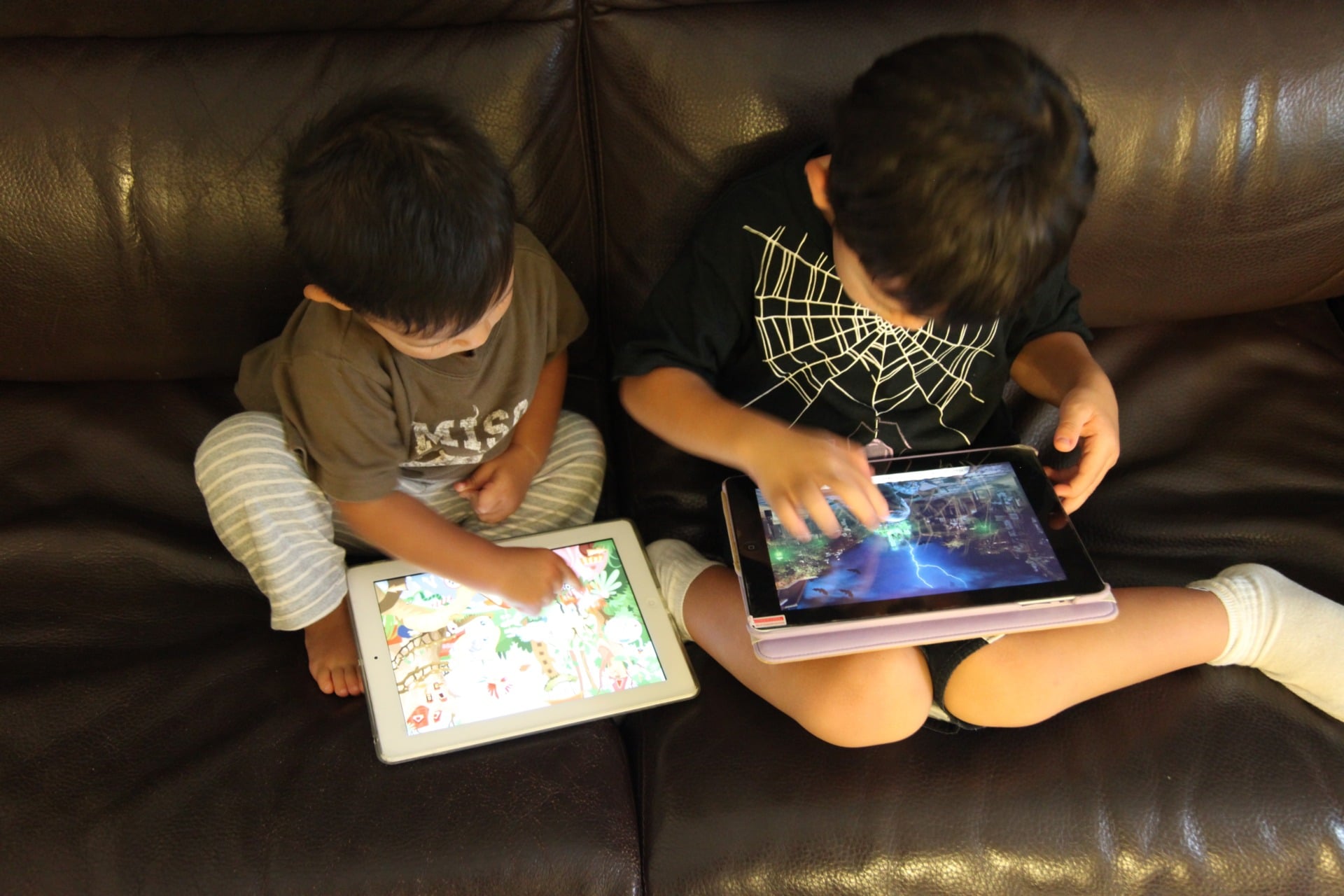two children sitting on a couch and playing games on an ipad