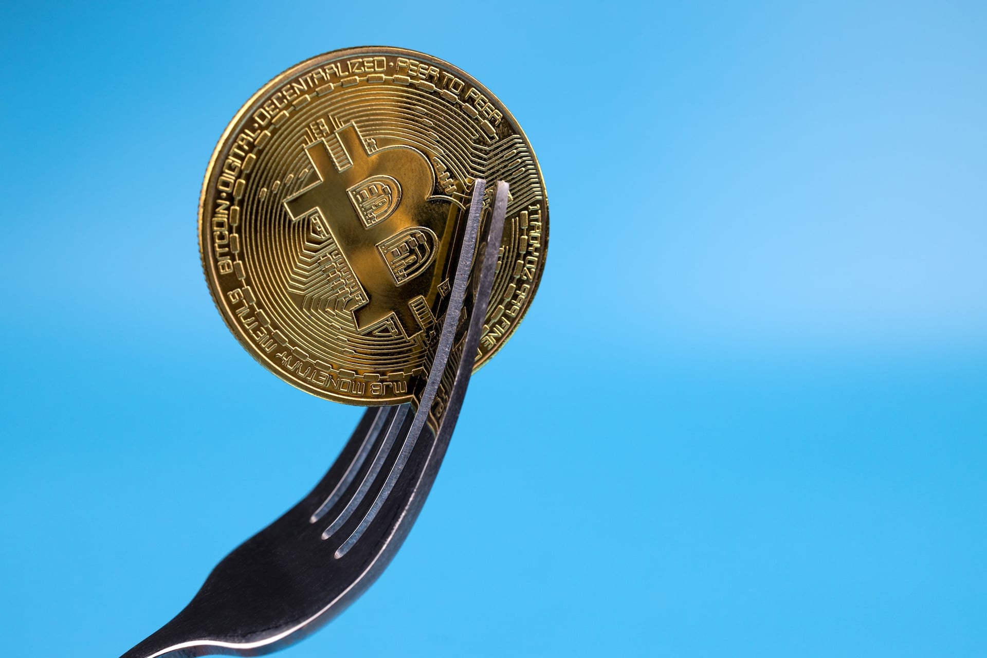 A prop bitcoin wedged between the tines of a literal fork illustrating the concept of a crypto fork.