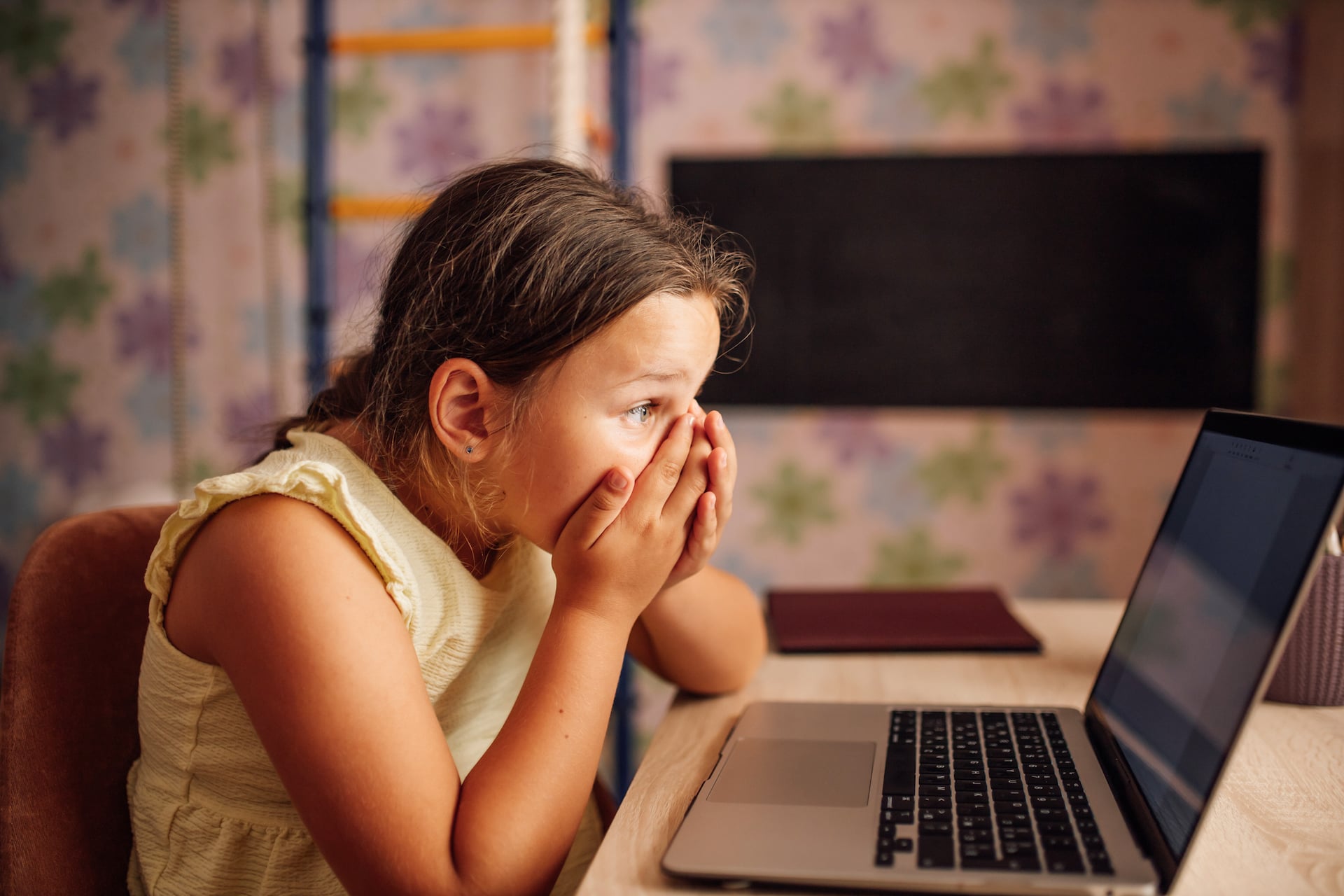 Preadolescent Girl Sitting At Desk Looking At Laptop Screen Covering Face With Hands