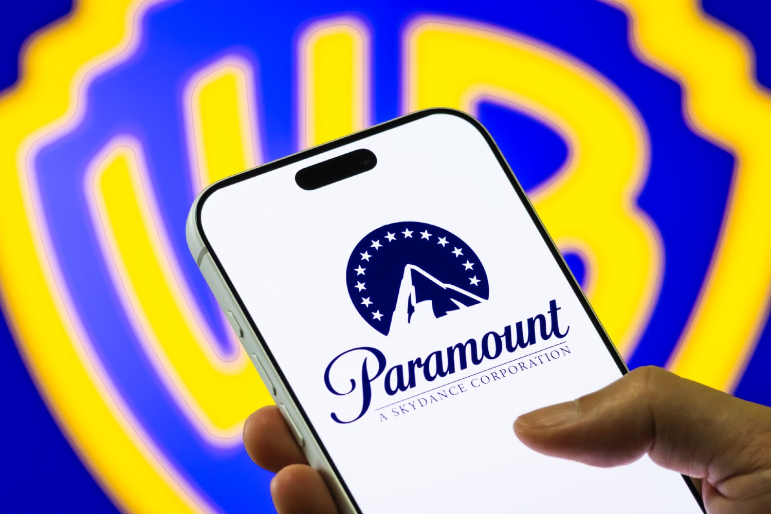 Paramount logo displayed on a smartphone in front of a background with the Warner Bros logo