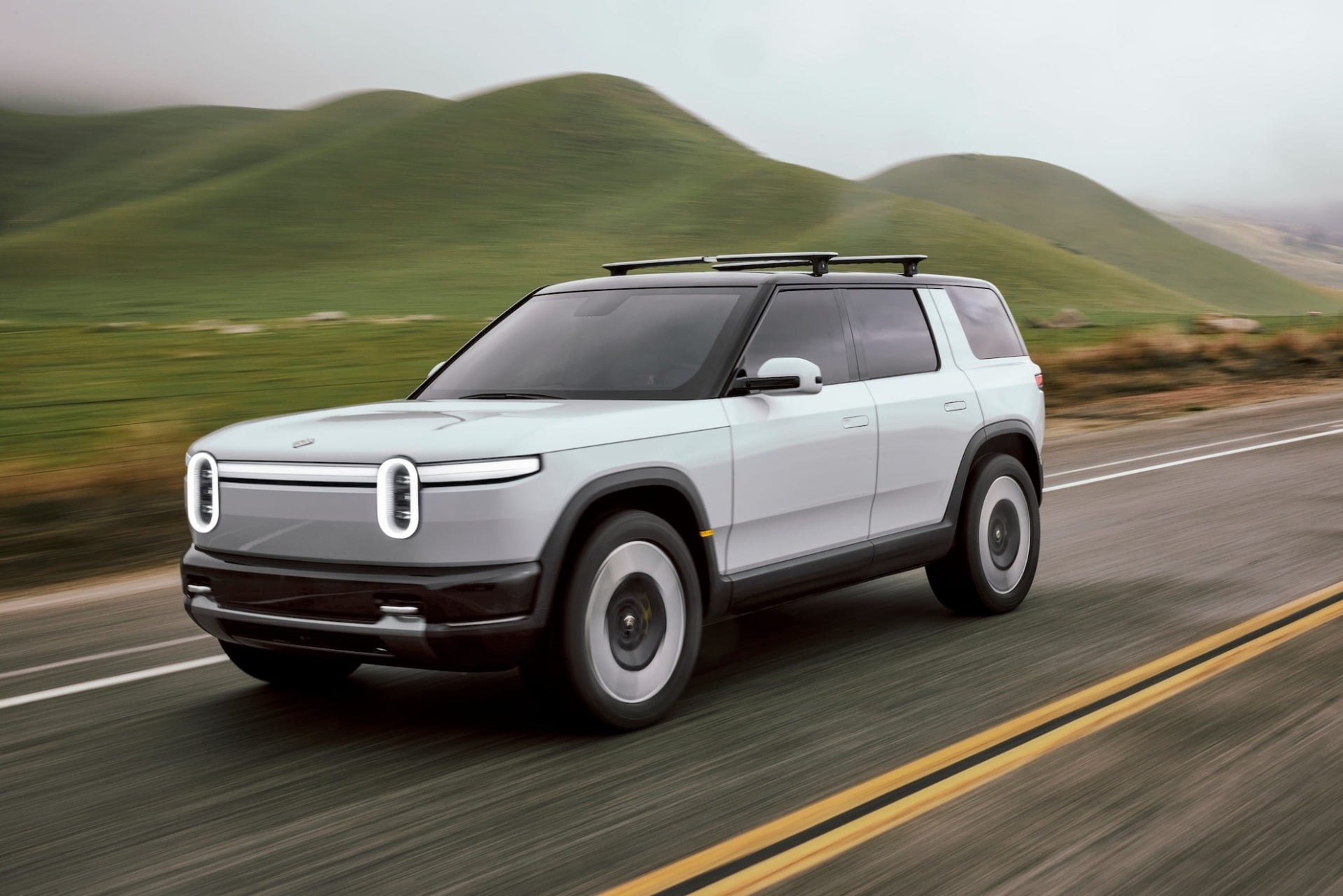 Rivian R2 SUV driving down rowad by hilss