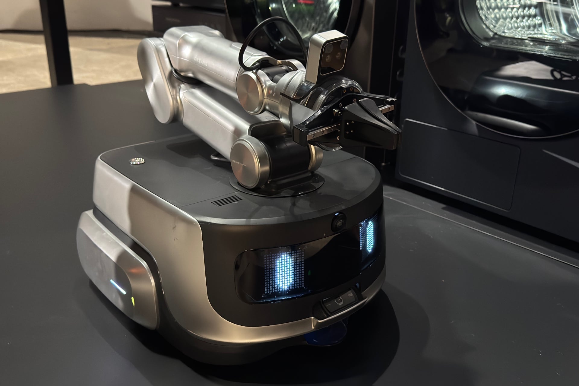 Il robot per lavanderia Z1 con il braccio robotico ripiegato. Una facciata in vetro è illuminata da due luci ovali blu che sembrano occhi.