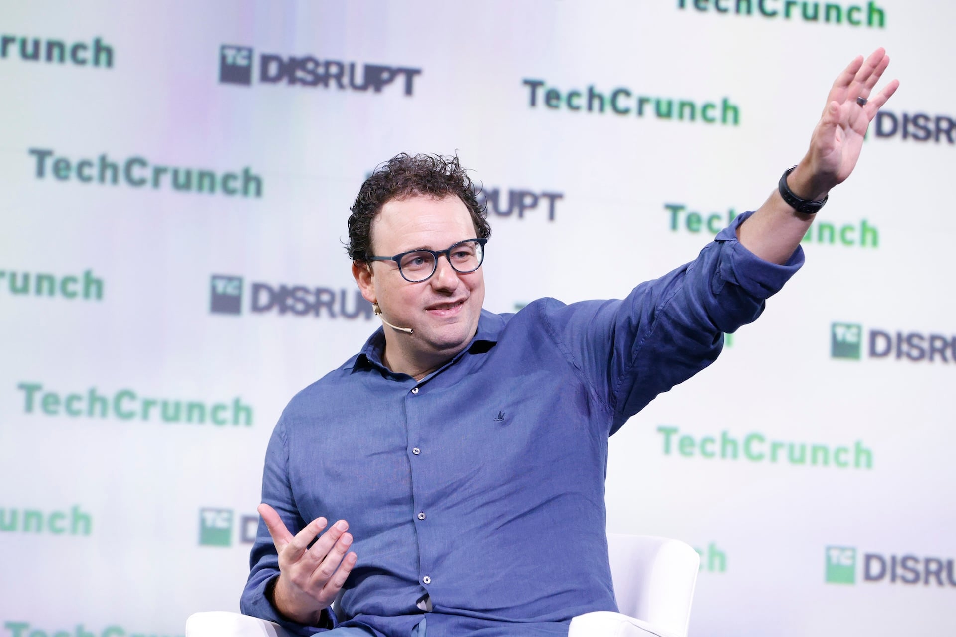 Dario Amodei, the CEO of Anthropic waving on a stage with "Techcrunch Disrupt 2023" written on the backdrop