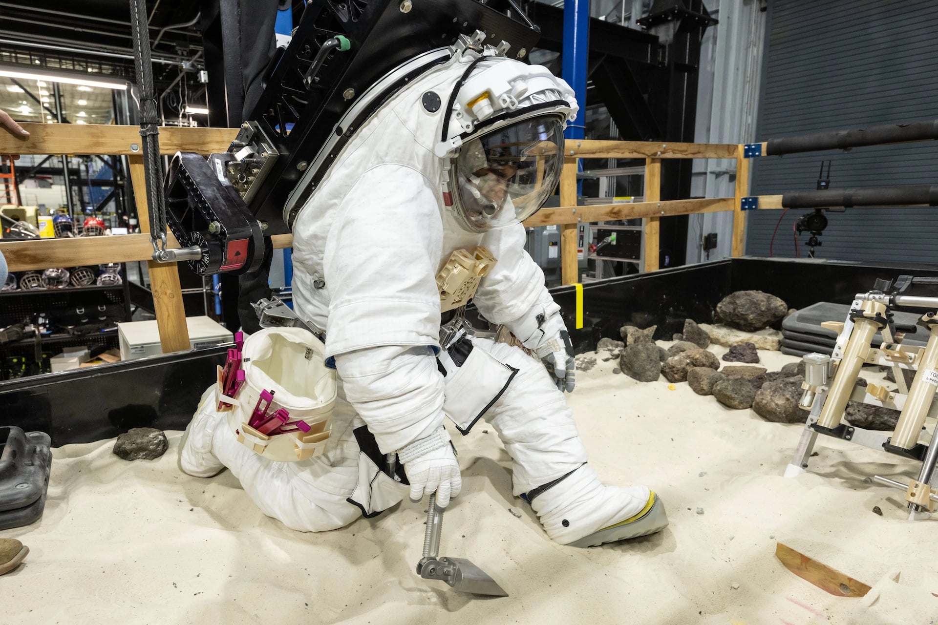 A NASA crew member practices using lunar tools to collect samples at NASA’s Johnson Space Center while wearing the AxEMU (Axiom Extravehicular Mobility Unit).