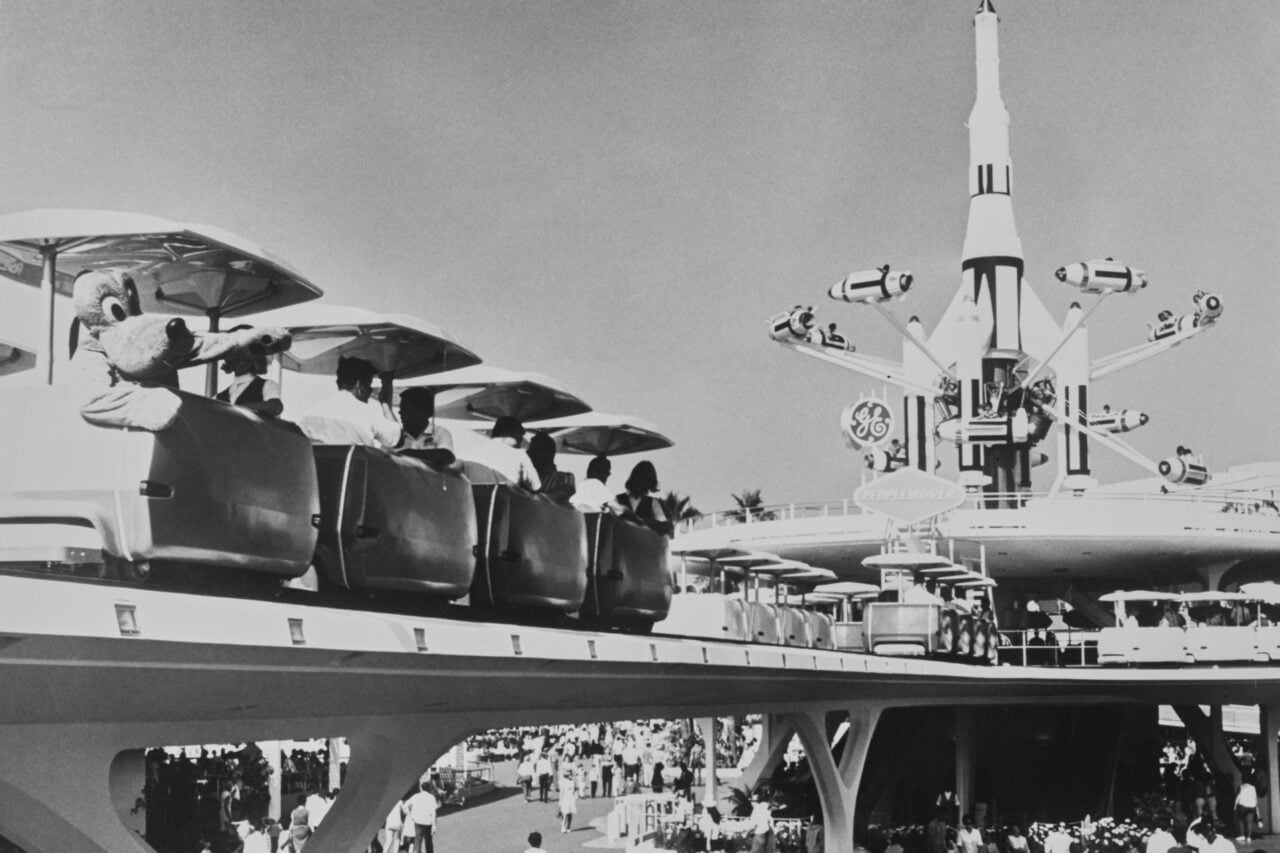 Disneyland visitors ride the PeopleMover in Tomorrowland, the Rocket Jets ride in the background, at Disneyland in Anaheim, California, July 1967. The transport ride saw Disneyland visitors ride small cars on tracks elevated above the Tomorrowland attraction.