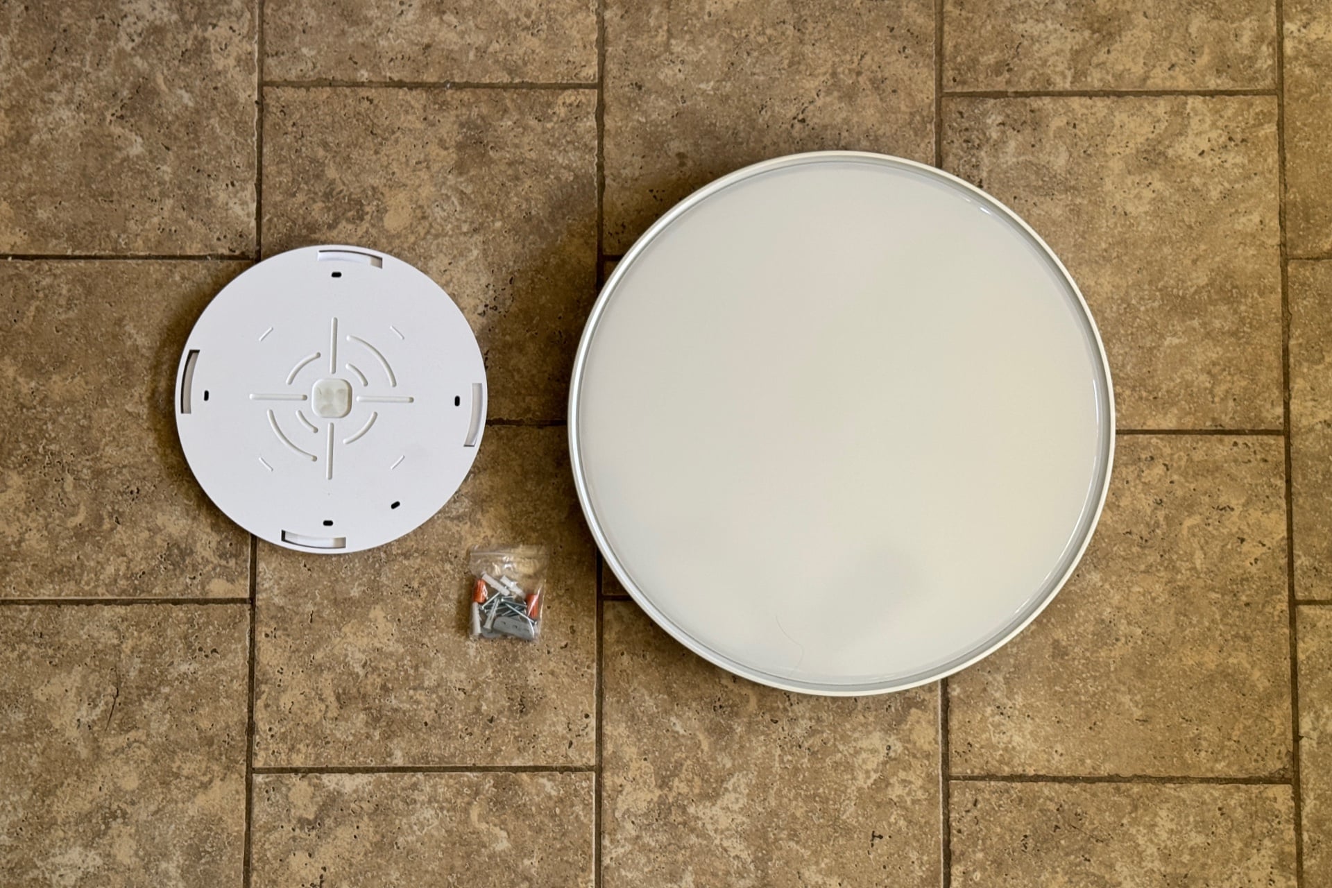 Pré-instalação do Plafon Govee Ultra, com a luminária colocada no chão próximo ao seu suporte e um saco de parafusos, porcas de arame e âncoras.