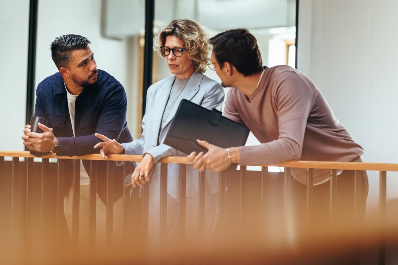 Three colleagues speaking at an office, one older woman and two younger men