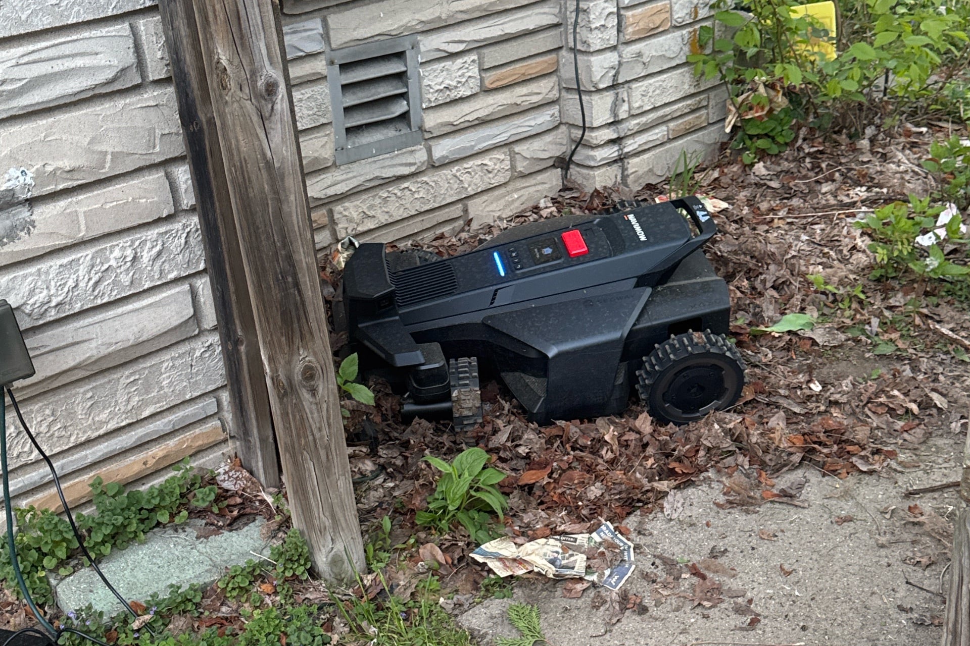Navimow X430 pointing into a corner and mired in leaves as it attempts to navigate through a gateway.