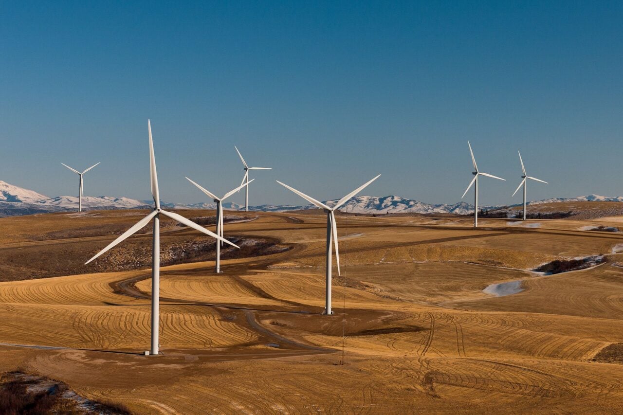 Wind turbines on a grassy plain with mountains in the background