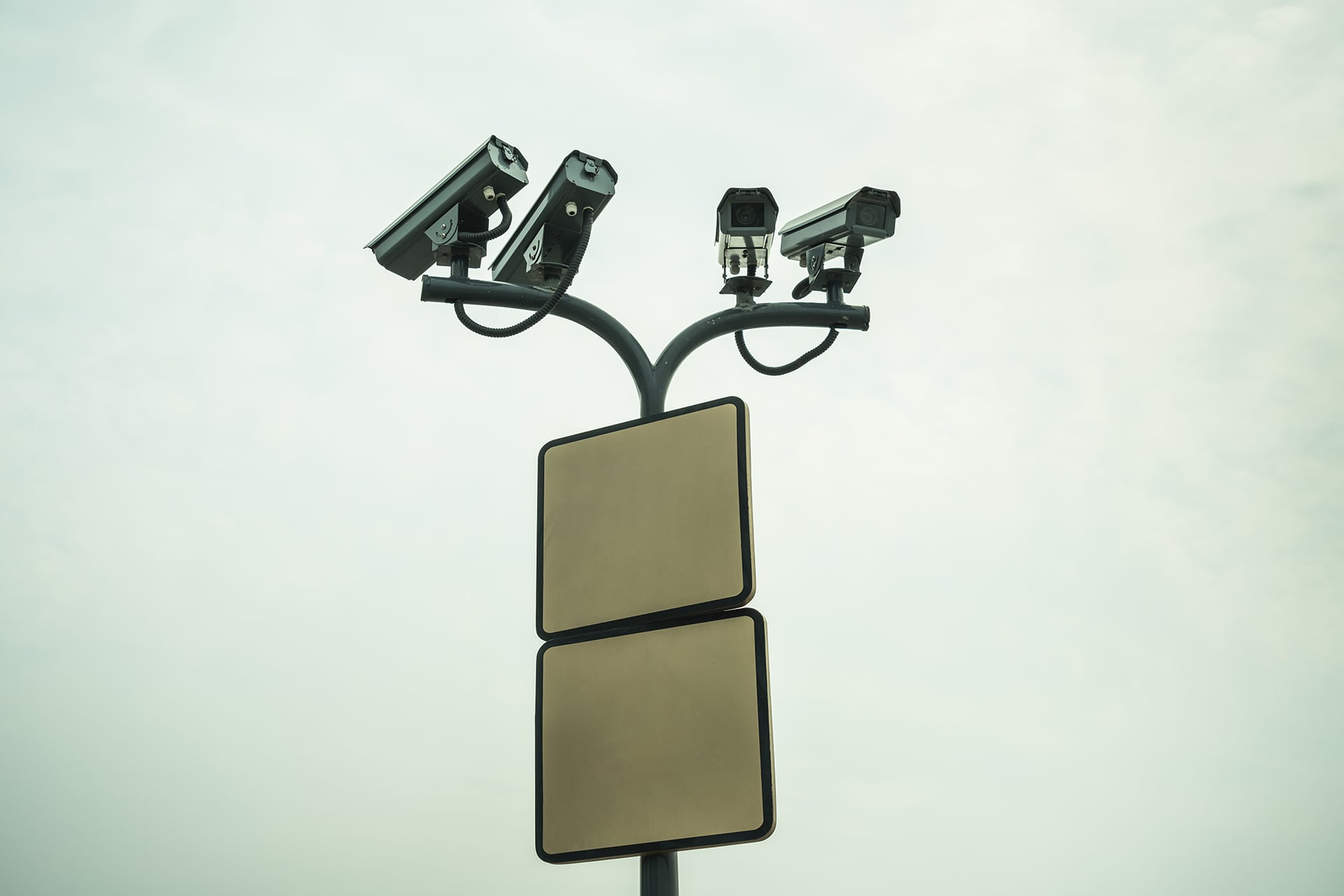Four surveillance cameras are seen on a pole against a cloudy sky.