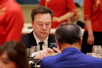 Elon Musk looking at his phone with furrowed brows at a dinner