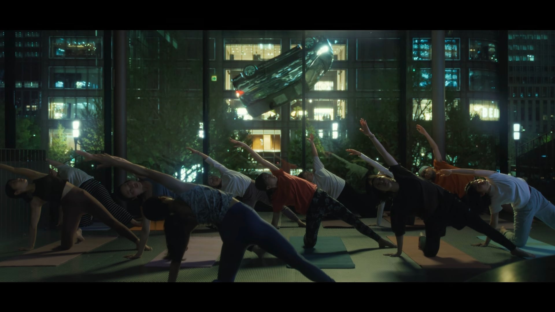 Human Vapor still of a car flyiing behind the window of a yoga class.