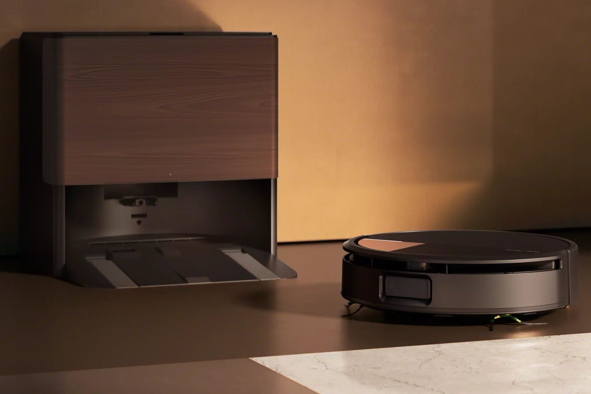 Roomba Max 775 sitting by its dock, which is large and has a woodgrain-patterned panel in front. The robot is black, with a gray, roughly triangular panel in its top front corner.