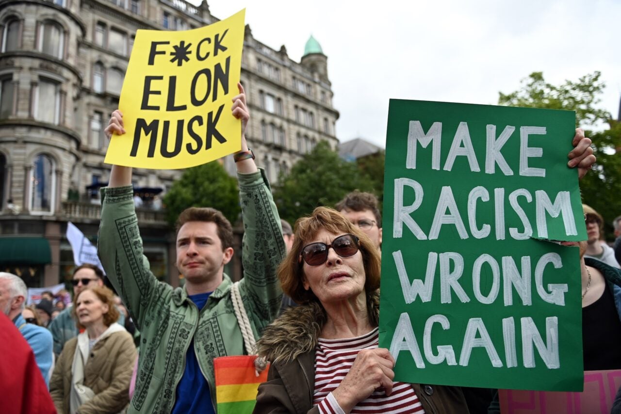 Demonstrators hold signs stating "f*ck Elon Musk" and "make racism wrong again" during a United Against Racism rally on June 13, 2026 in Belfast, Northern Ireland.
