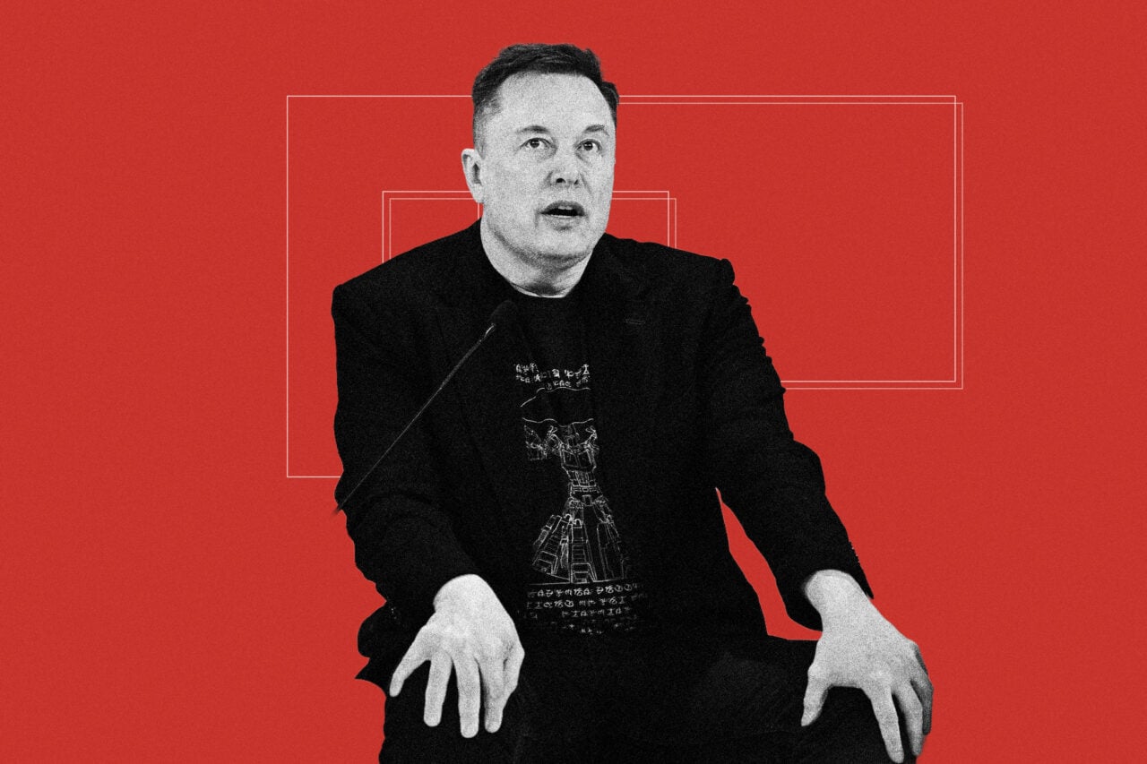 Elon Musk seen speaking at a conference against a red background.